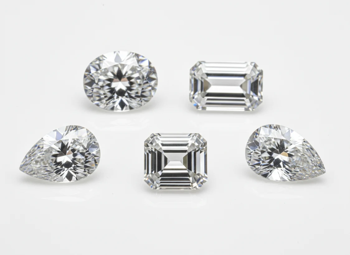 Moissanite gemstones in round, emerald, and pear cuts photographed on a light background